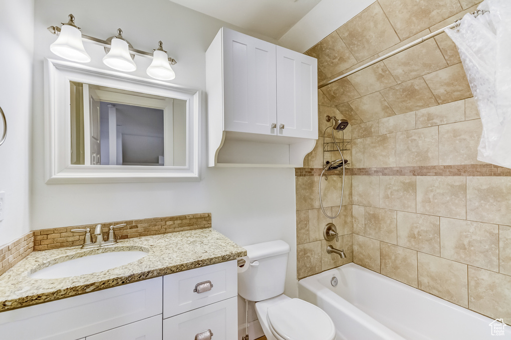 Bathroom with shower / bathtub combination with curtain, vanity, toilet, and tasteful backsplash