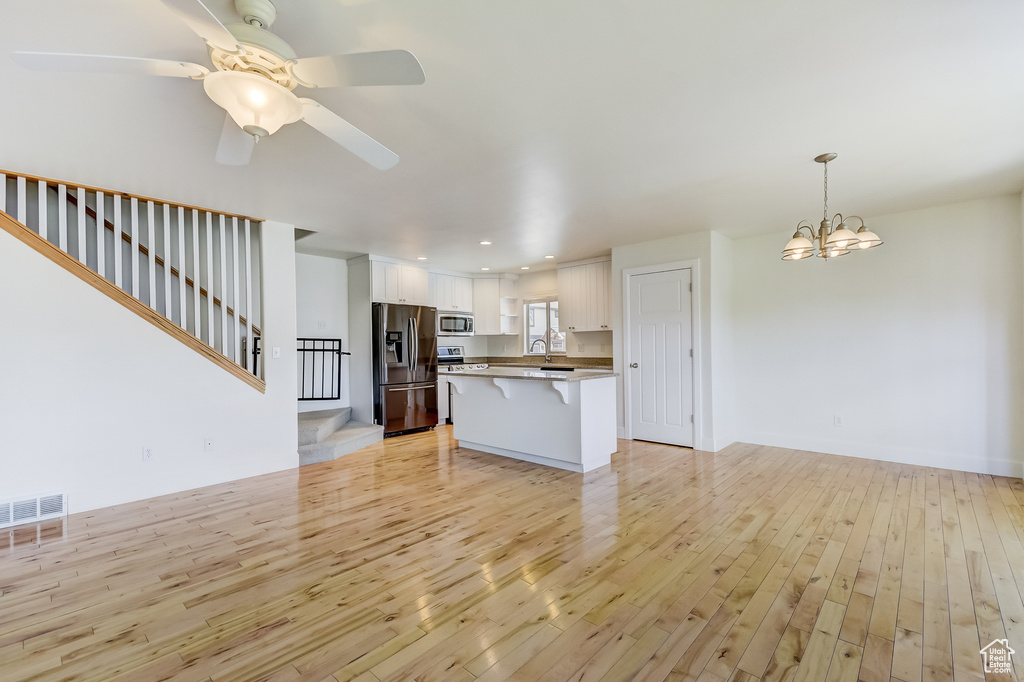 Unfurnished living room featuring recessed lighting, stairs, light wood-style floors, ceiling fan with notable chandelier, and visible vents