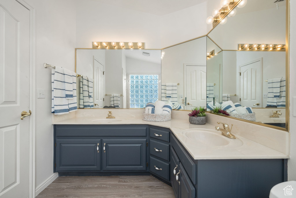 Full bath with a sink, double vanity, and wood finished floors