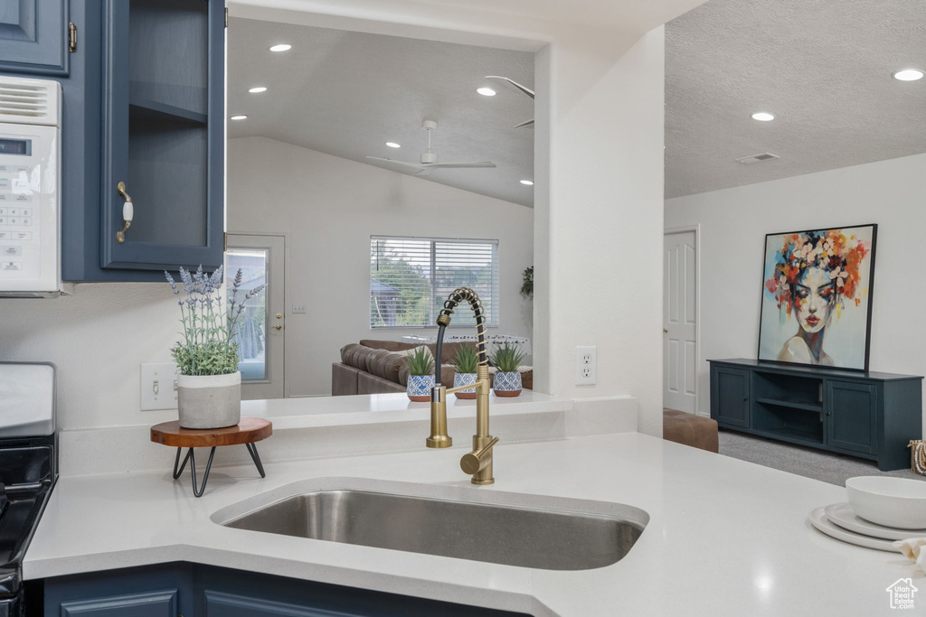 Kitchen with light countertops, a sink, white microwave, and blue cabinetry
