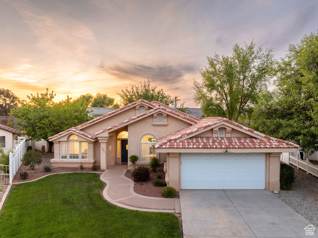 Mediterranean / spanish-style house with fence, stucco siding, concrete driveway, a yard, and a tile roof
