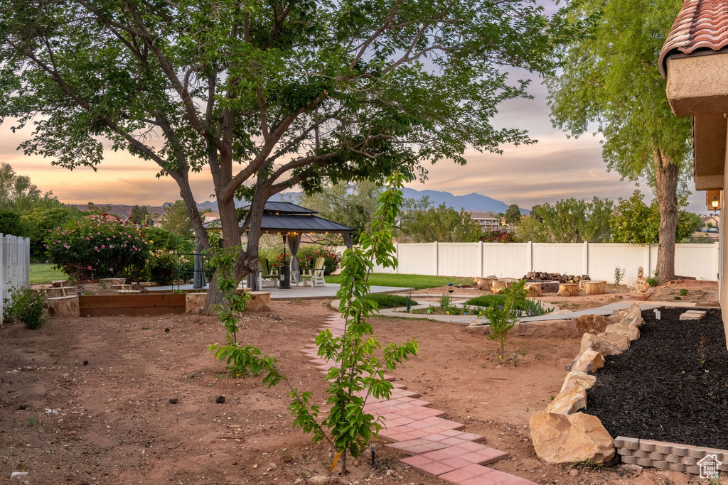 Yard at dusk featuring a patio, a fenced backyard, a vegetable garden, a gazebo, and a mountain view
