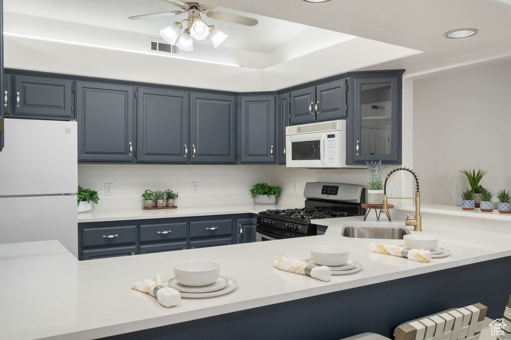 Kitchen featuring a sink, white appliances, blue cabinetry, a ceiling fan, and visible vents
