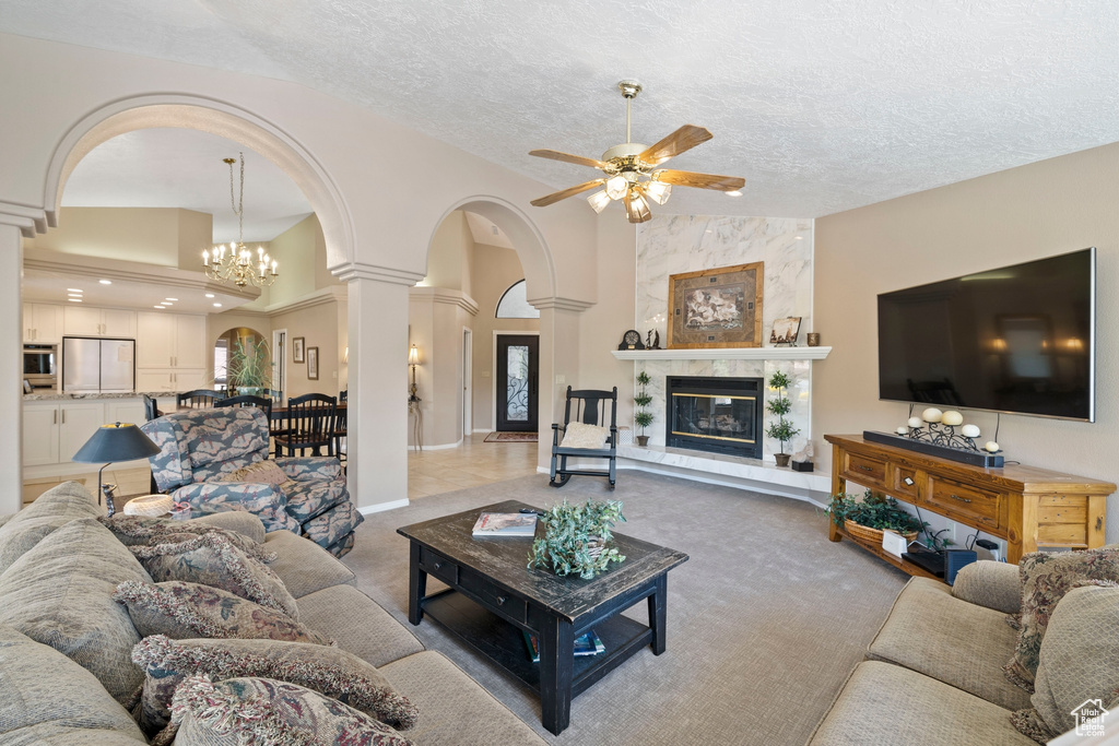 Carpeted living room featuring decorative columns, a textured ceiling, a high end fireplace, arched walkways, and ceiling fan with notable chandelier