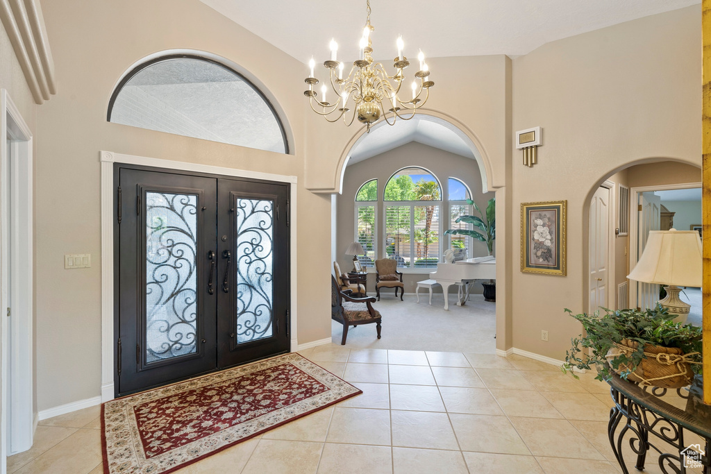 Entryway featuring light tile patterned floors, high vaulted ceiling, french doors, and a notable chandelier