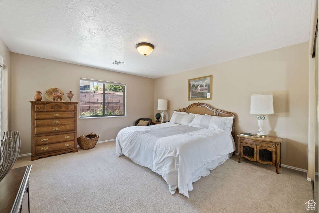 Bedroom featuring a textured ceiling, baseboards, visible vents, and light carpet