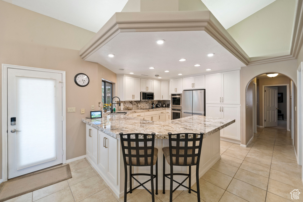 Kitchen with appliances with stainless steel finishes, arched walkways, light stone countertops, a peninsula, and light tile patterned flooring