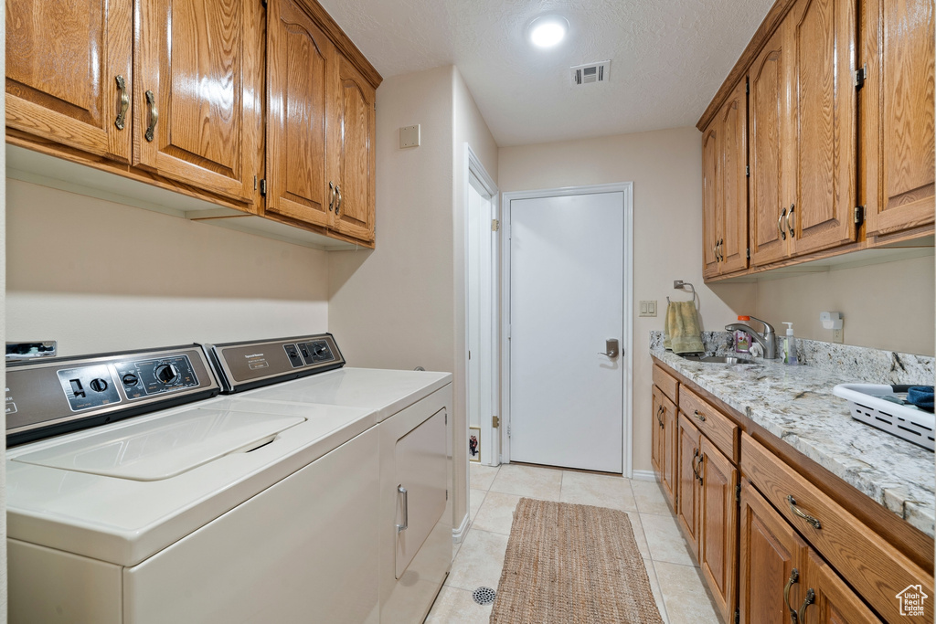 Clothes washing area featuring visible vents, washing machine and clothes dryer, a sink, cabinet space, and light tile patterned floors