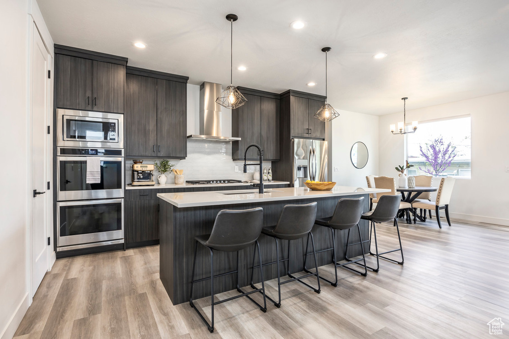 Kitchen featuring wall chimney range hood, a sink, light countertops, a breakfast bar area, and stainless steel appliances