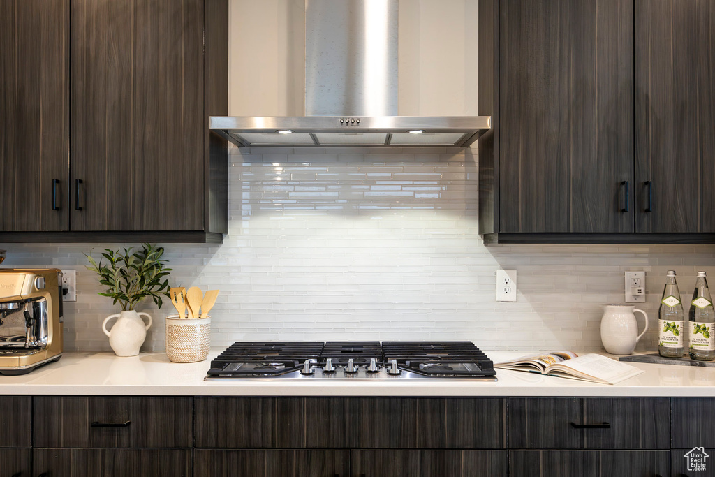Kitchen with wall chimney range hood, light countertops, backsplash, and dark brown cabinets