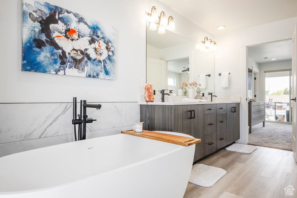 Bathroom with recessed lighting, double vanity, wood finished floors, and a soaking tub
