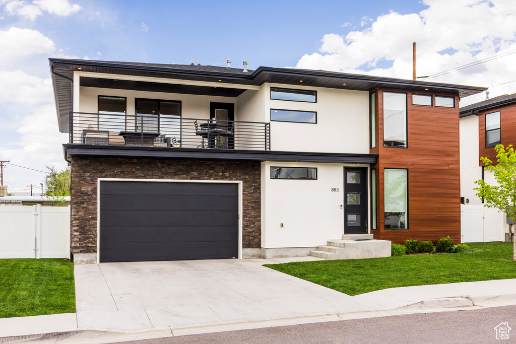 Modern home with a garage, fence, a balcony, a front lawn, and concrete driveway