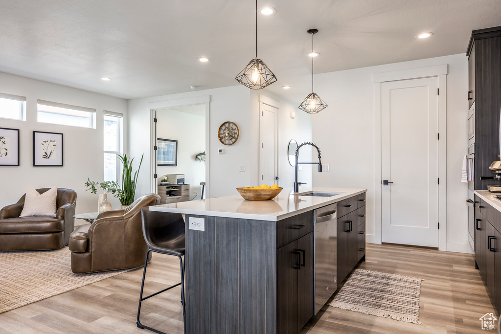 Kitchen with a center island with sink, light countertops, a sink, light wood finished floors, and appliances with stainless steel finishes