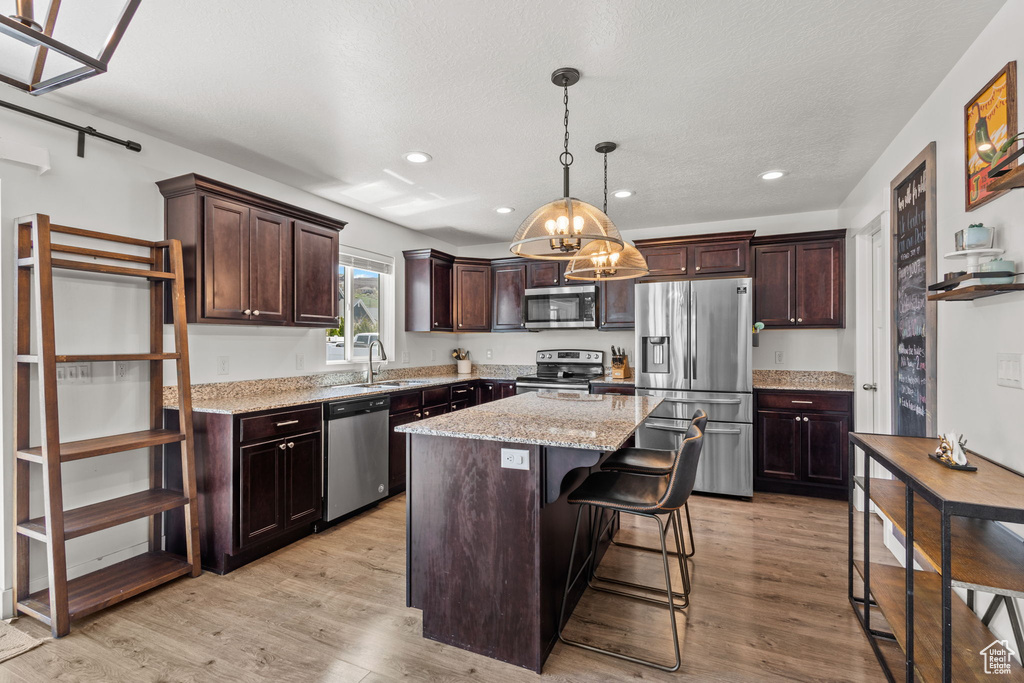 Kitchen with dark brown cabinets, a center island, appliances with stainless steel finishes, a notable chandelier, and decorative light fixtures