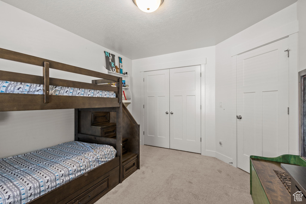 Bedroom featuring a textured ceiling, light colored carpet, and a closet