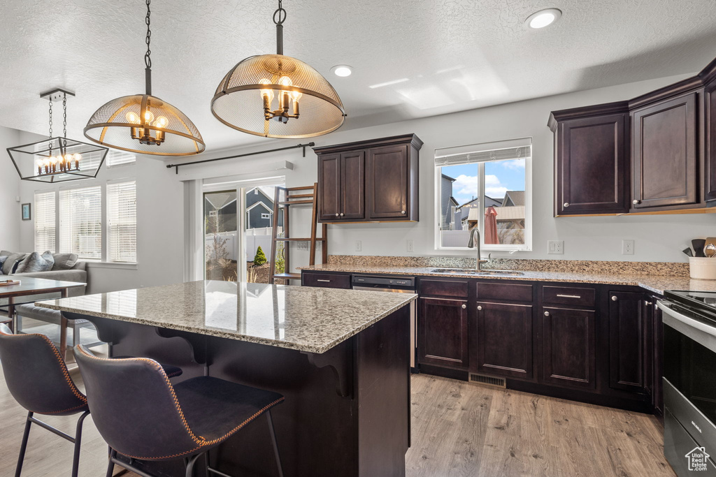 Kitchen with electric range, an inviting chandelier, light stone counters, a sink, and plenty of natural light