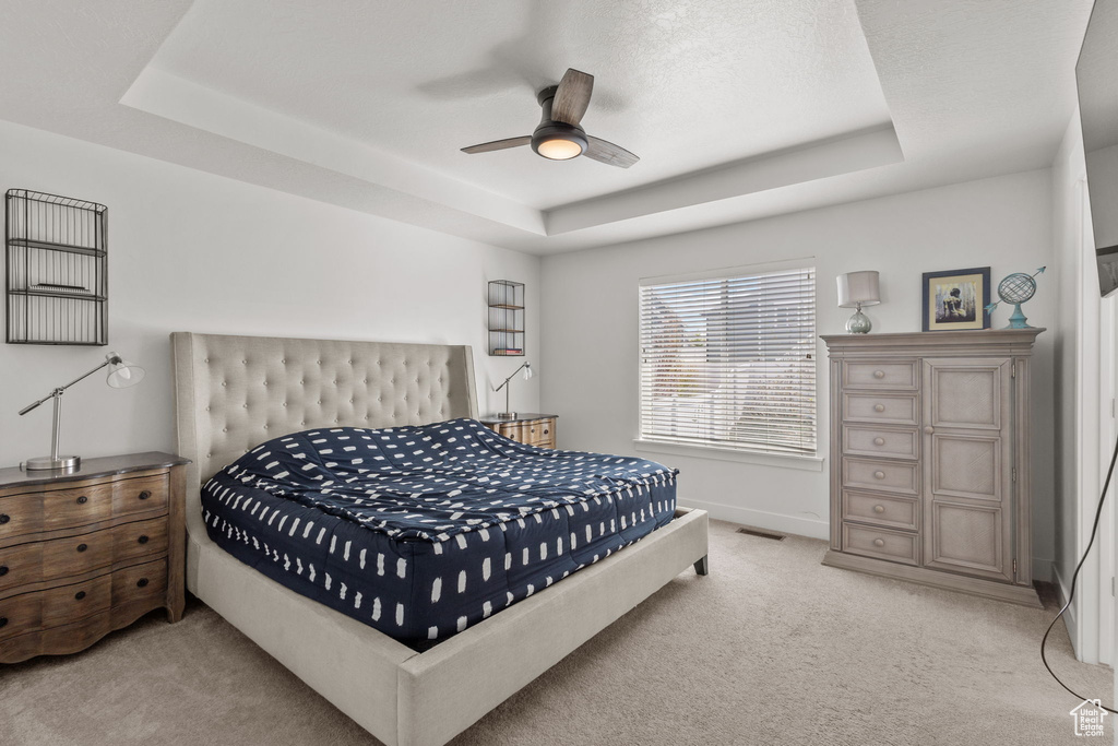 Bedroom featuring a ceiling fan, visible vents, light colored carpet, baseboards, and a tray ceiling