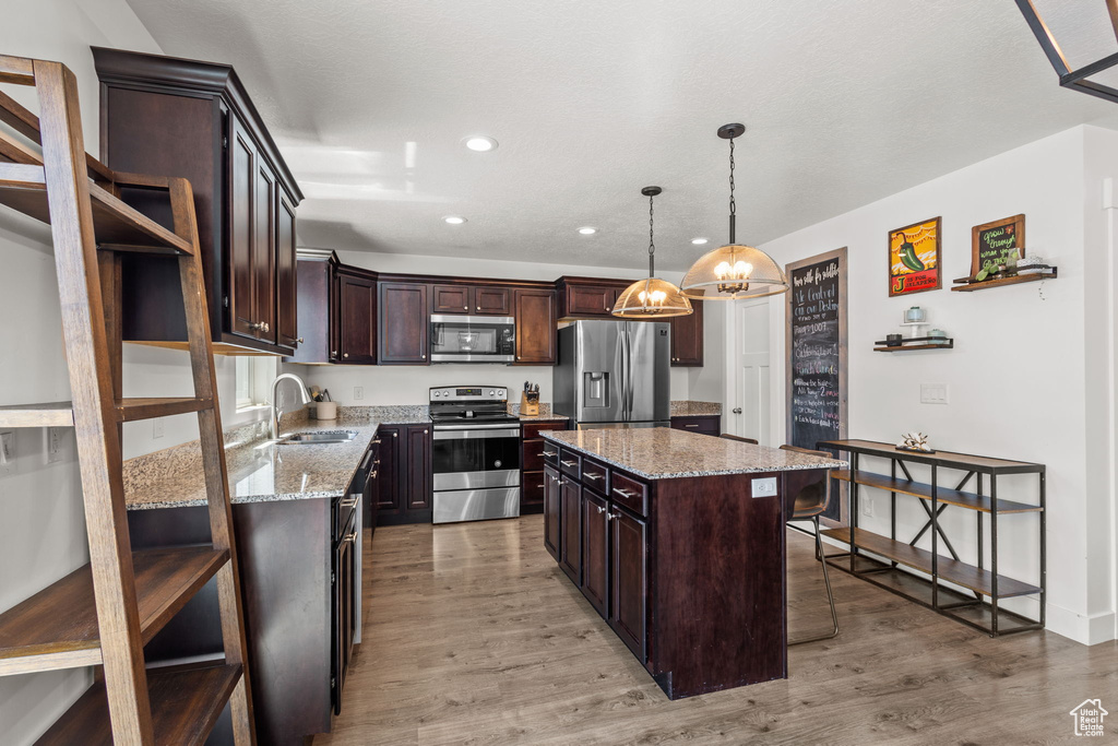 Kitchen featuring dark brown cabinets, a sink, light wood finished floors, a breakfast bar, and stainless steel appliances