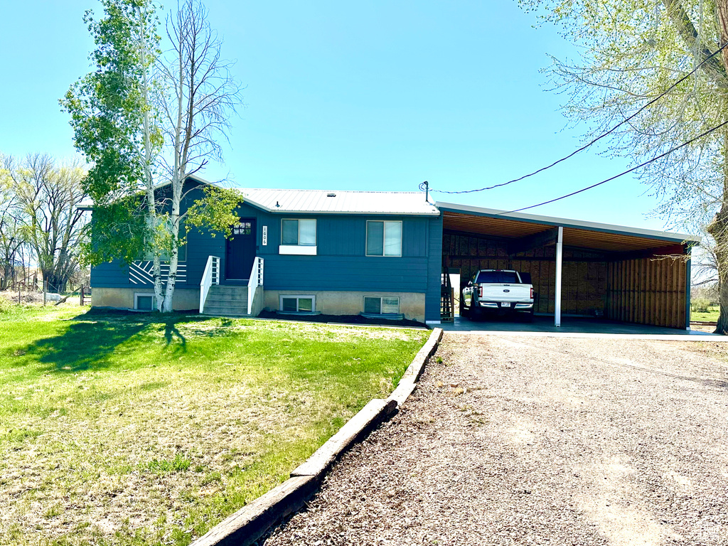 View of front of house featuring driveway, metal roof, a front yard, and an attached carport