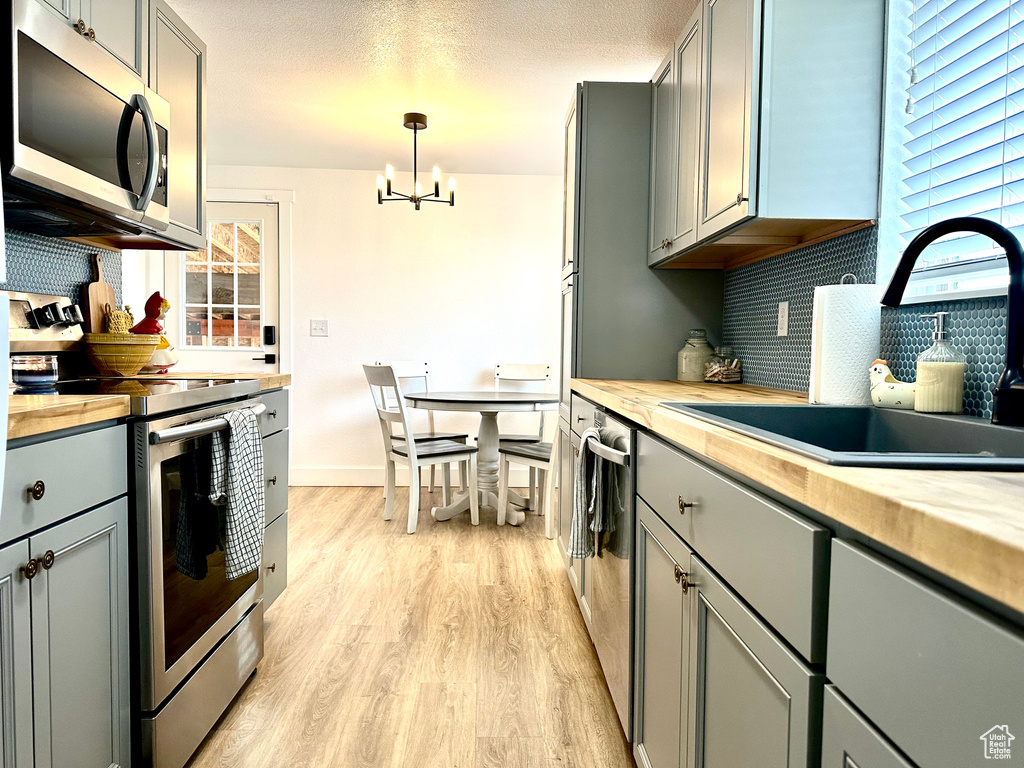 Kitchen featuring butcher block countertops, gray cabinets, a sink, appliances with stainless steel finishes, and a notable chandelier