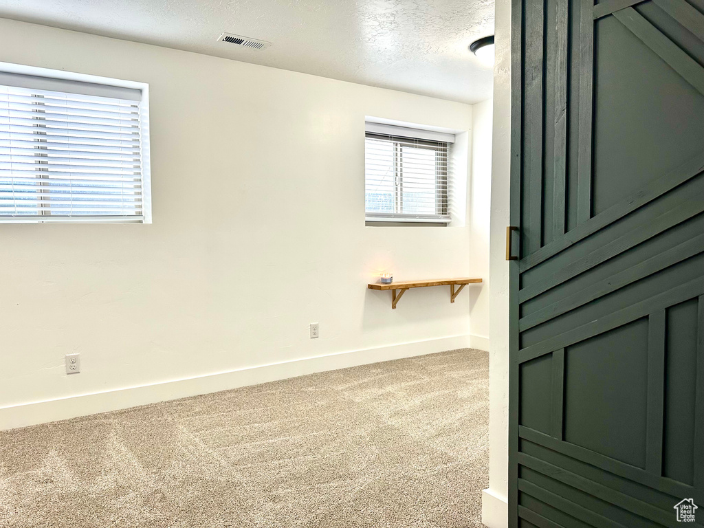 Carpeted spare room featuring baseboards, a textured ceiling, and visible vents