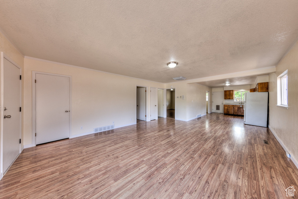 Unfurnished living room with baseboards, a textured ceiling, visible vents, and light wood-style flooring