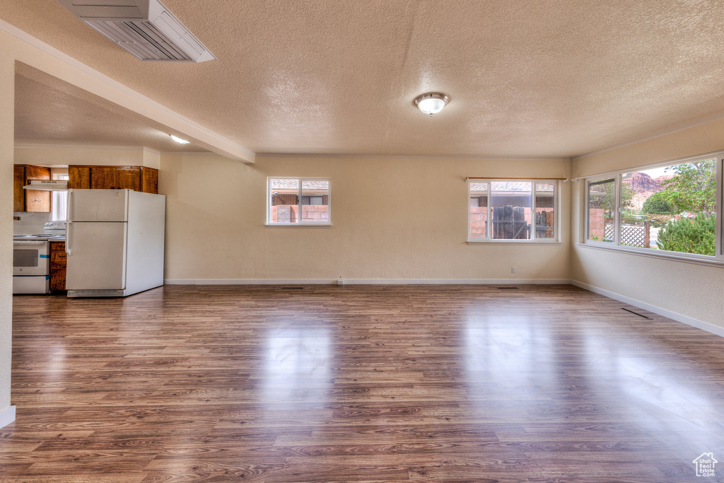 Unfurnished living room featuring a healthy amount of sunlight, baseboards, a textured ceiling, and wood finished floors