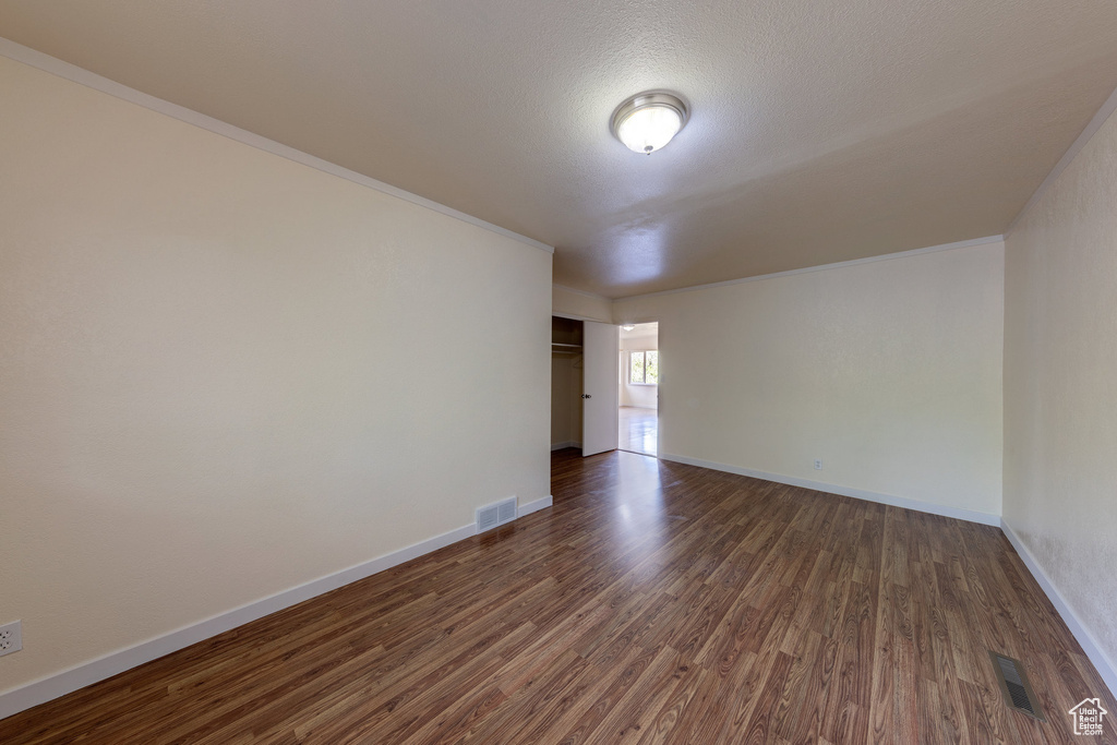 Empty room featuring baseboards, dark wood-type flooring, and visible vents