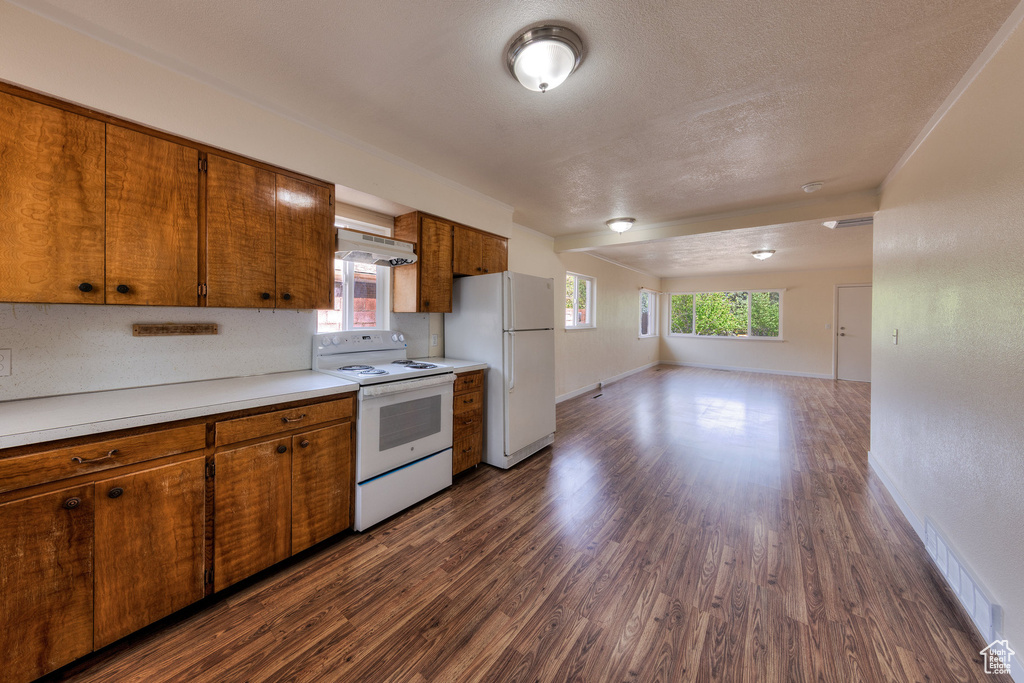 Kitchen featuring visible vents, white appliances, dark wood-type flooring, light countertops, and brown cabinets