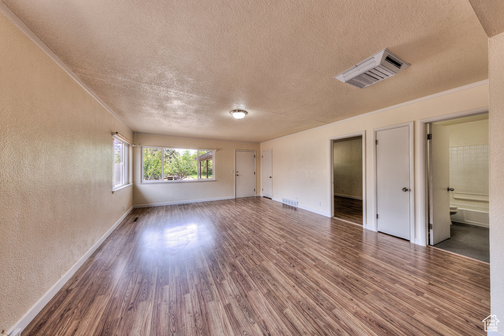 Empty room featuring a textured wall, a textured ceiling, and wood finished floors