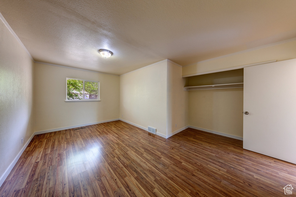Unfurnished bedroom featuring a textured ceiling, visible vents, wood finished floors, baseboards, and a closet