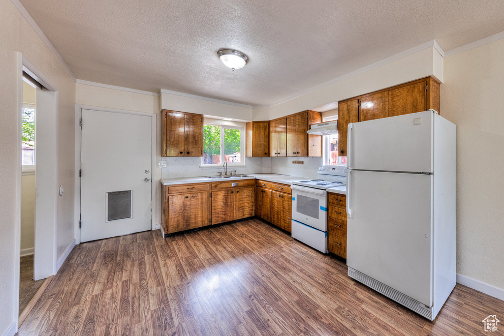 Kitchen with a textured ceiling, light countertops, a sink, under cabinet range hood, and white appliances
