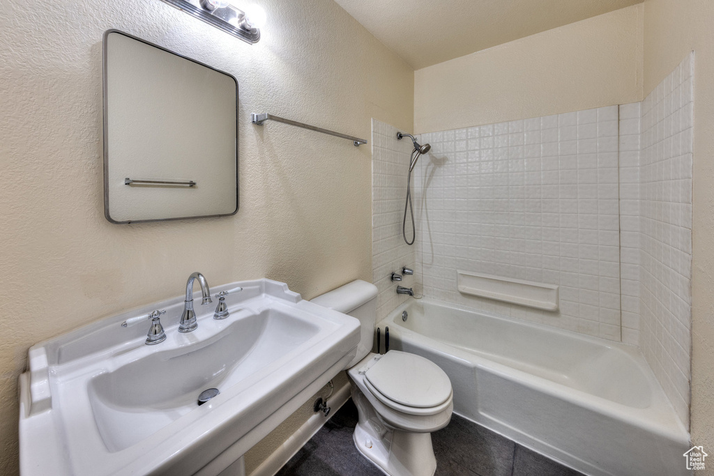 Bathroom featuring a sink, a textured wall, shower / bathtub combination, and toilet
