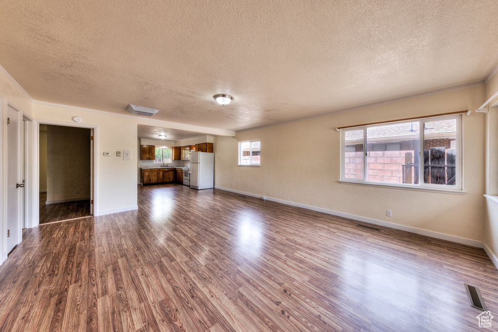 Unfurnished living room with baseboards, dark wood-style flooring, a textured ceiling, and visible vents