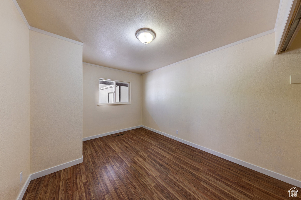 Empty room with a textured ceiling, baseboards, ornamental molding, and dark wood-type flooring