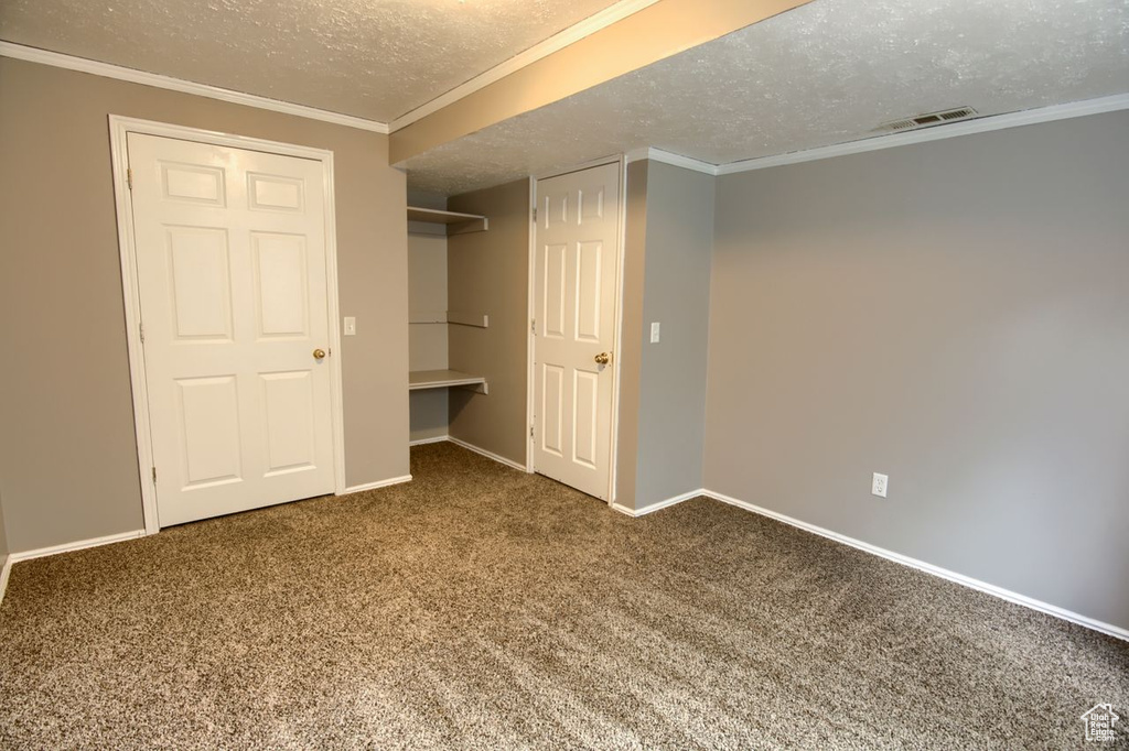Unfurnished bedroom featuring carpet floors, ornamental molding, visible vents, baseboards, and a textured ceiling