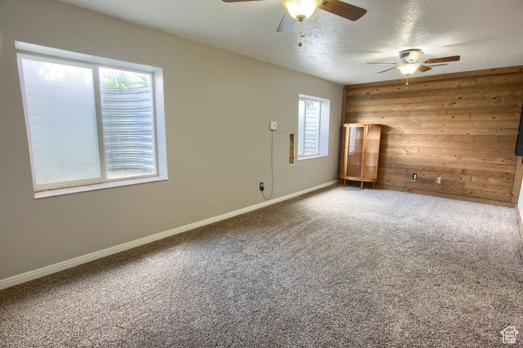 Empty room with baseboards, carpet flooring, ceiling fan, and wooden walls