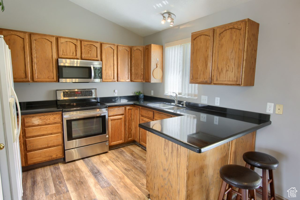 Kitchen featuring appliances with stainless steel finishes, a sink, a peninsula, lofted ceiling, and light wood-style floors