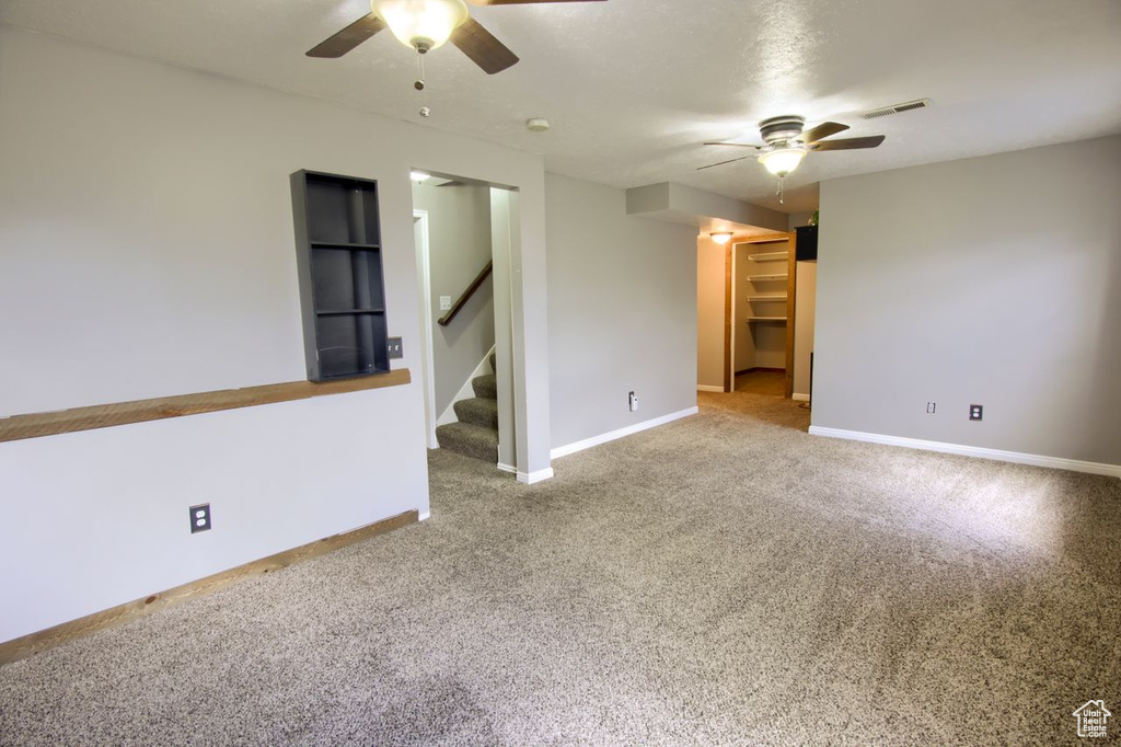 Carpeted spare room featuring baseboards, ceiling fan, stairs, and visible vents