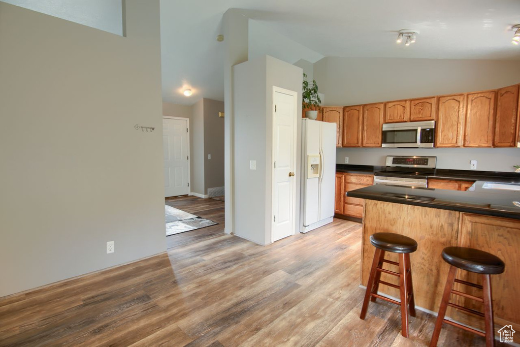 Kitchen with dark countertops, high vaulted ceiling, a kitchen bar, light wood-type flooring, and stainless steel appliances