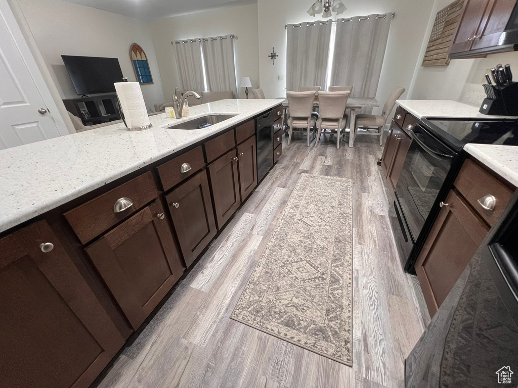 Kitchen featuring electric range oven, a sink, light stone counters, black dishwasher, and light wood-style flooring
