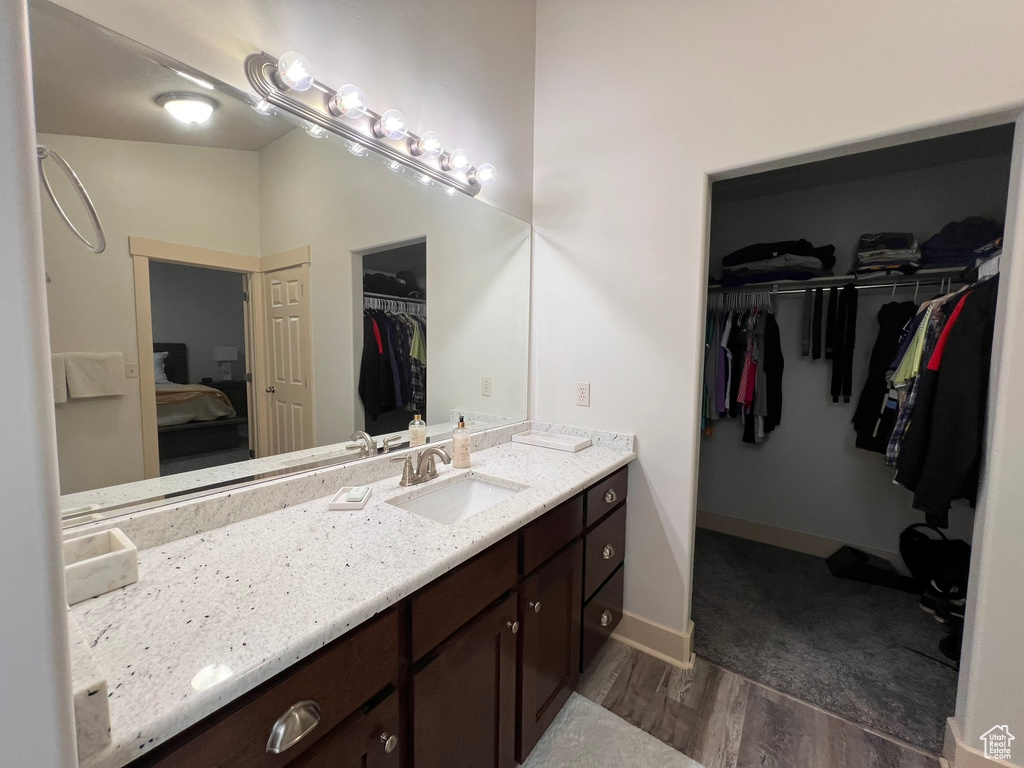 Ensuite bathroom featuring a walk in closet, ensuite bath, vanity, baseboards, and wood finished floors