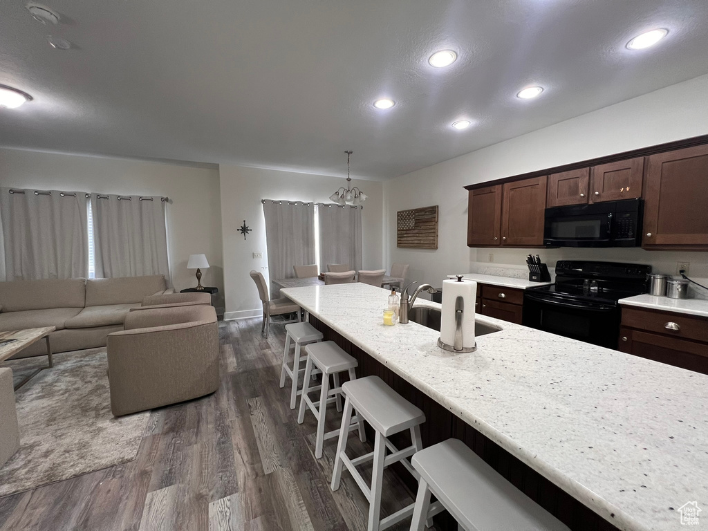Kitchen featuring dark brown cabinets, a kitchen bar, recessed lighting, dark wood finished floors, and black appliances