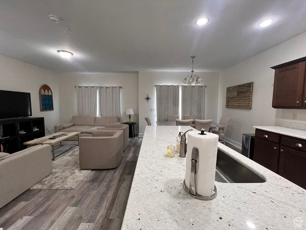 Kitchen with dark wood-style flooring, dark brown cabinets, an inviting chandelier, a sink, and open floor plan