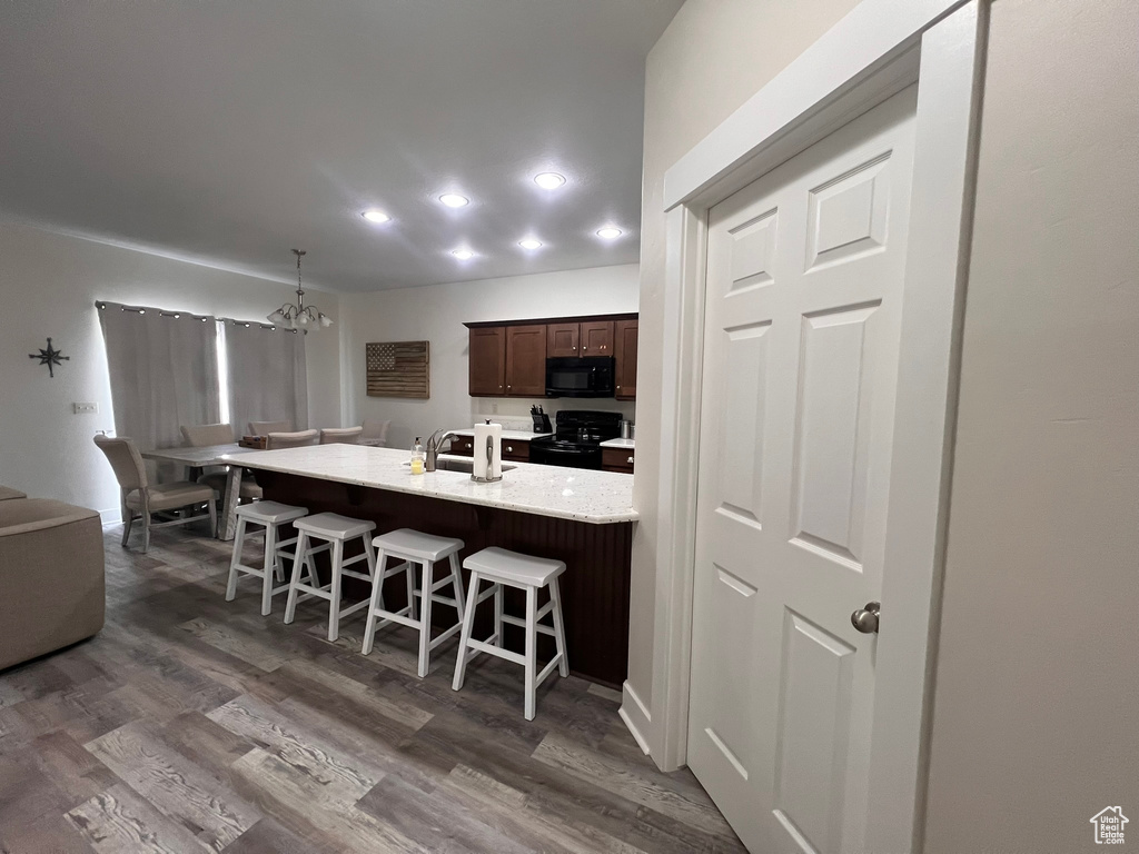 Kitchen featuring dark wood-style flooring, a kitchen bar, dark brown cabinets, black appliances, and an inviting chandelier