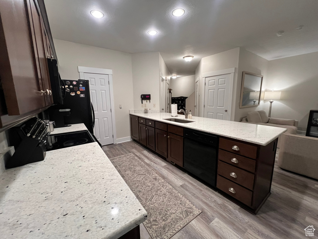 Kitchen with dark brown cabinetry, a sink, a peninsula, wood finished floors, and black appliances
