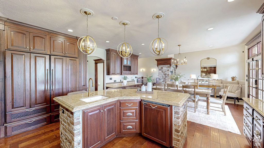 Kitchen with a sink, arched walkways, a chandelier, an island with sink, and dark wood finished floors