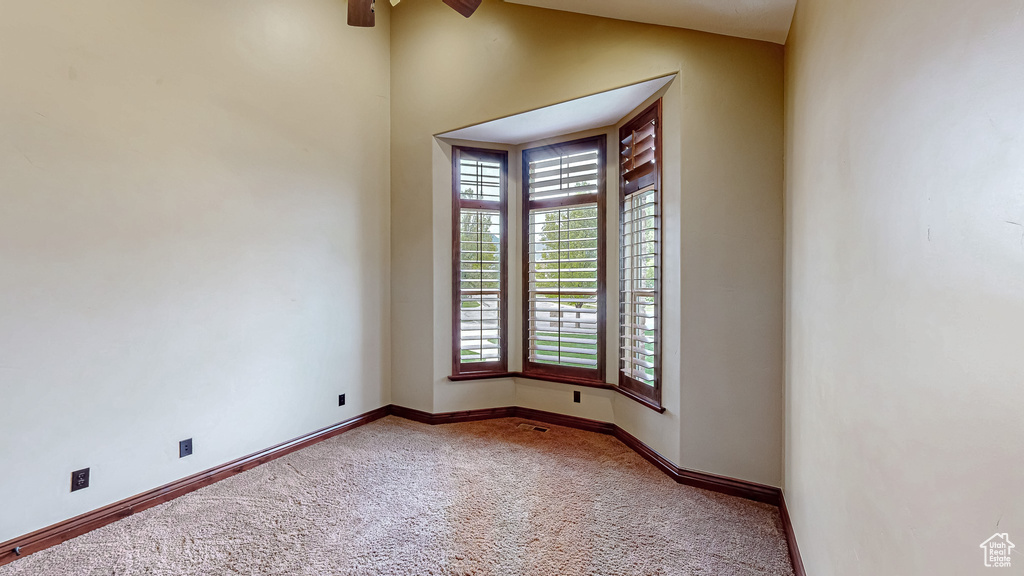 Carpeted spare room with vaulted ceiling, baseboards, and a ceiling fan