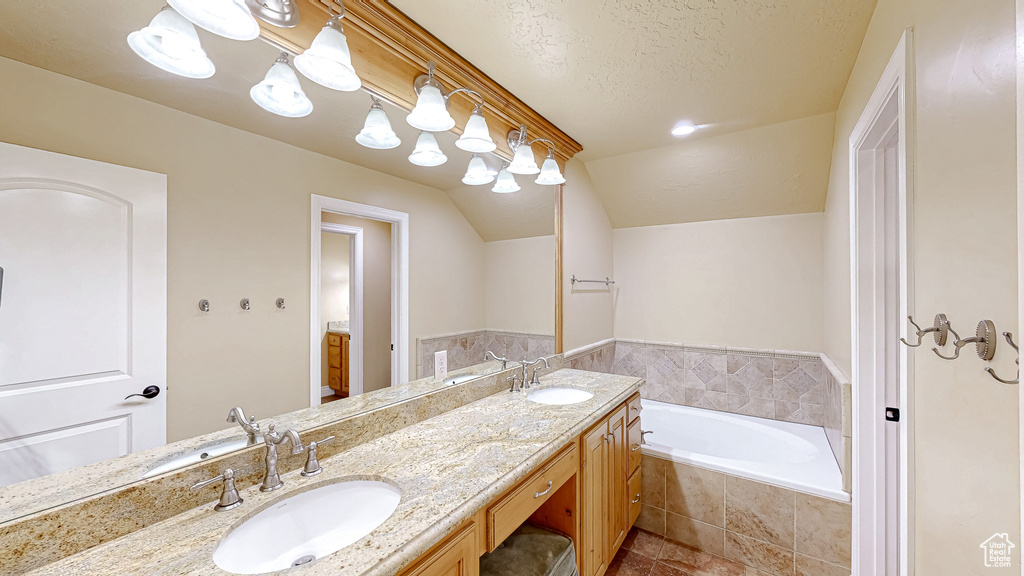 Bathroom featuring double vanity, lofted ceiling, a sink, and a bath