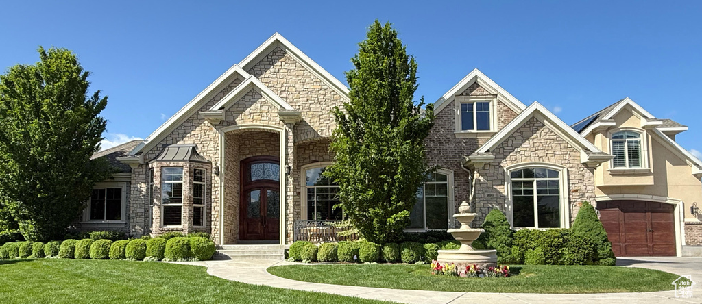 French country inspired facade featuring stone siding, a front lawn, and driveway